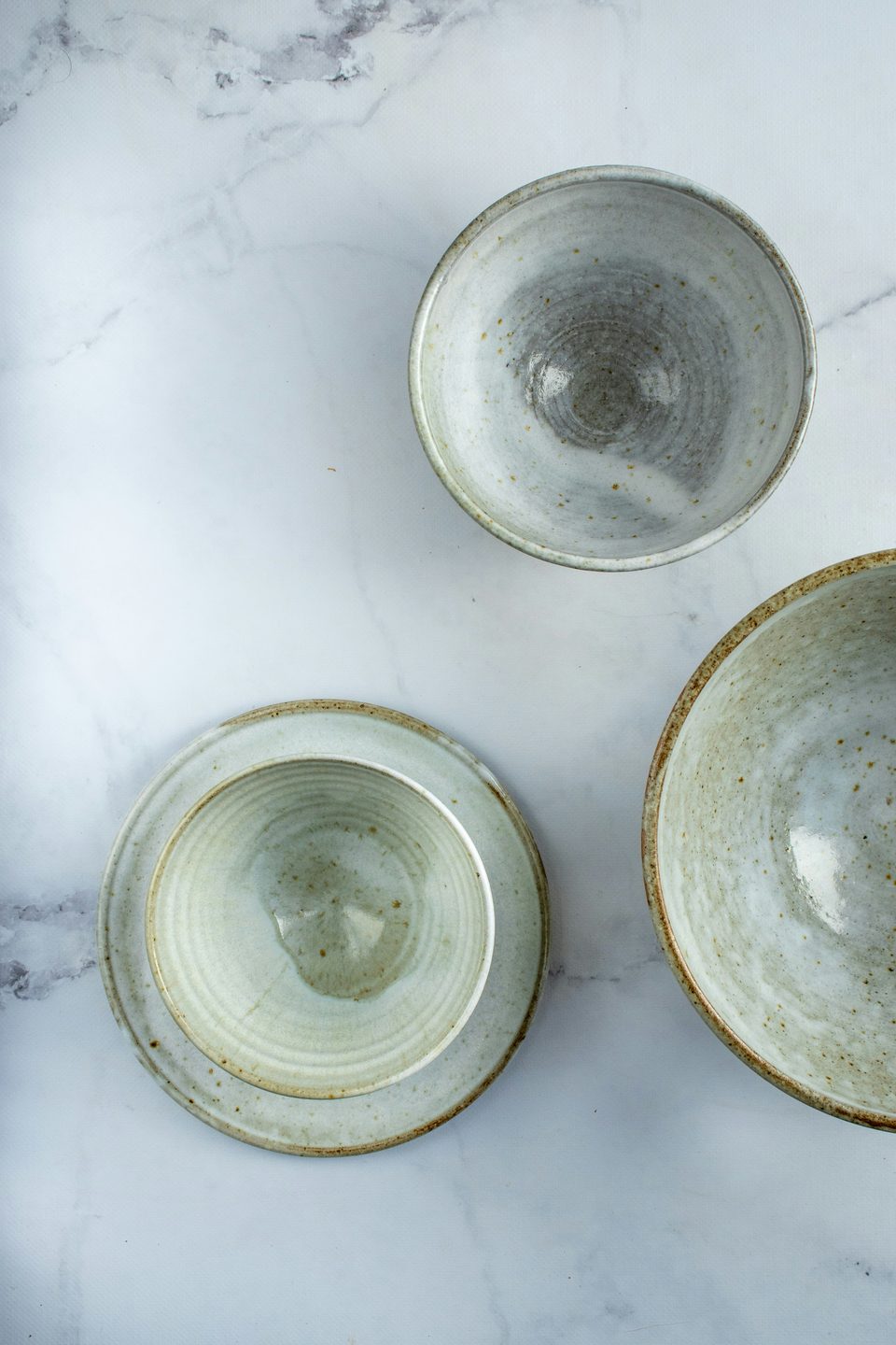 Tres bowls pequeños de cerámica esmaltada en verde grisáceo sobre mármol, vistos desde arriba.