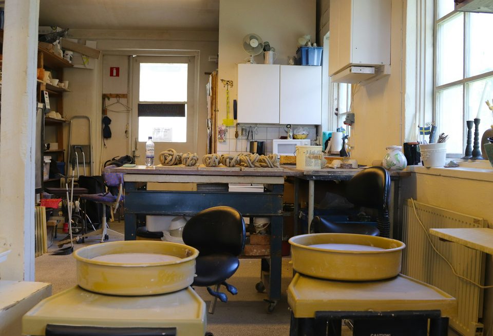 Taller de cerámica con dos tornos, mesas de trabajo y estantes con piezas. (en el taller)