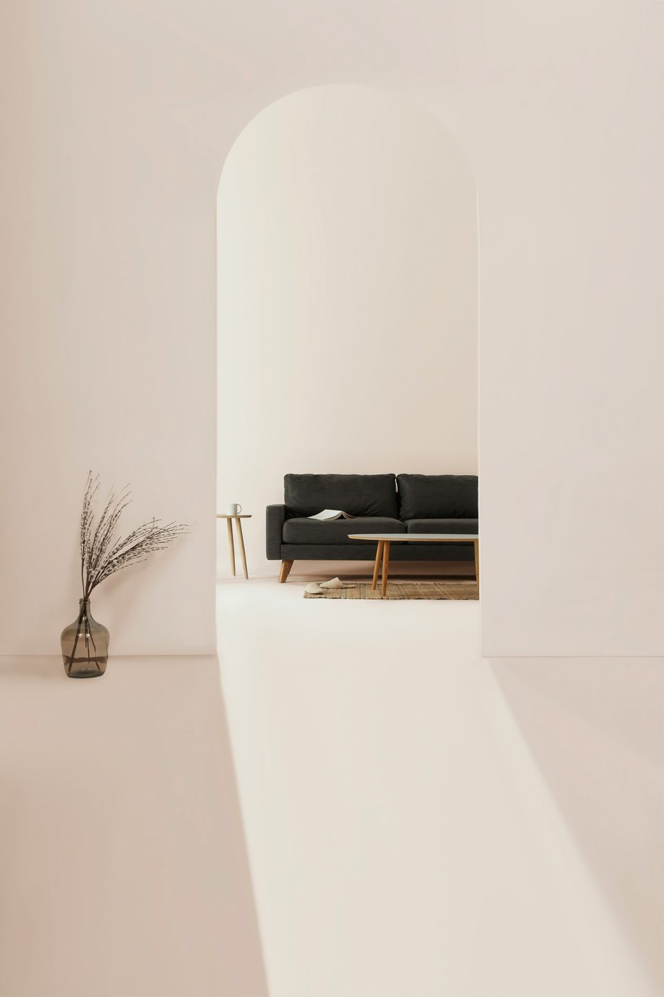 Vano en arco en un muro claro que deja ver una sala con un sofá oscuro y una franja de luz sobre el piso.