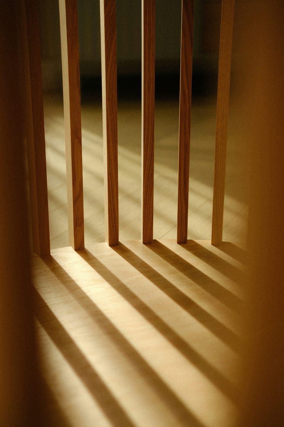 Listones de madera que proyectan franjas de sombra sobre una superficie clara.