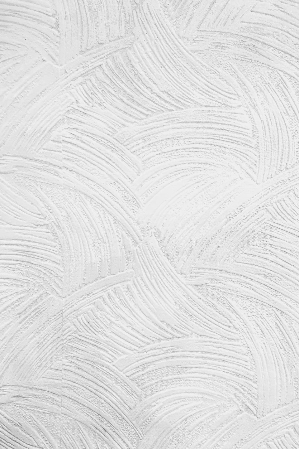Detalle de un muro blanco con aplanado texturizado en trazos curvos.