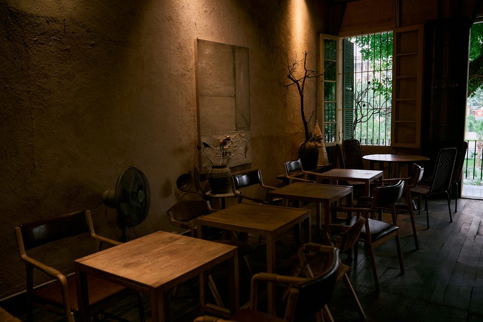 Interior de una cafetería con mesas, sillas y luz natural.